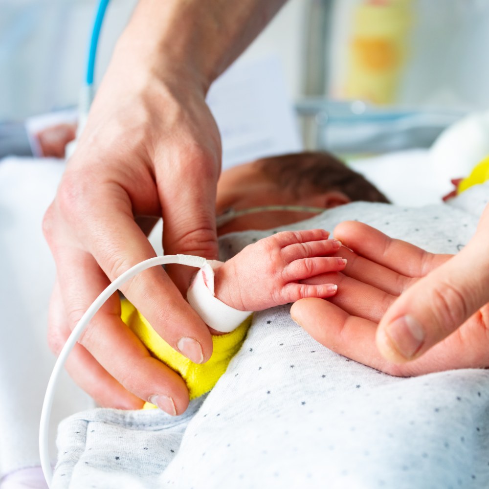 Parent helping neonatal infant to grasp fingertip in incubator