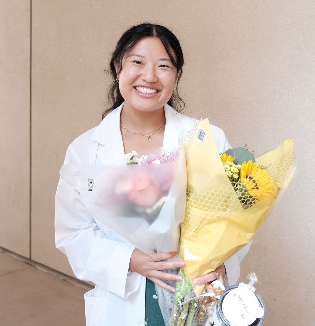 Mercy Deng stands smiling wearing a white coat and holding flowers.