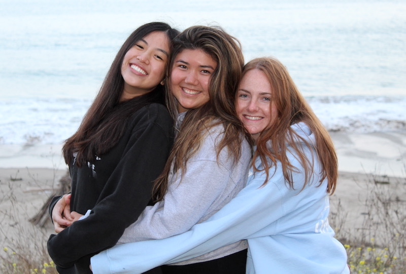 Three young women smiling for a picture at the beach