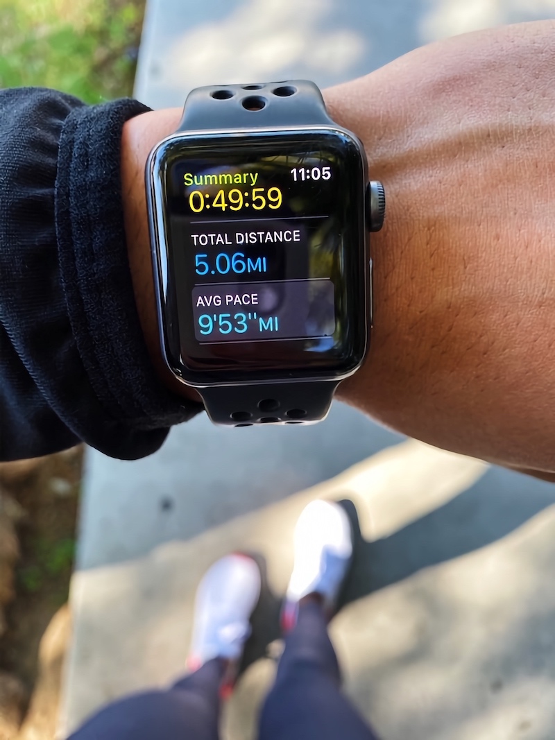 Pictured is an Apple Watch with the distance of 5 miles, pace 9 minutes and 53 seconds, and total run time 49 minutes and 59 seconds.