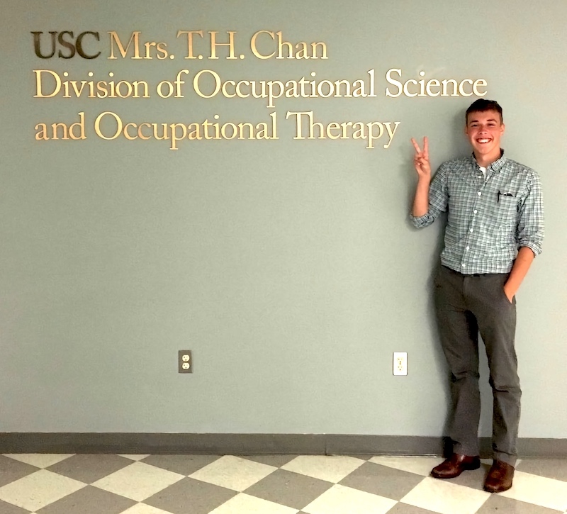 A young man holding up a peace sign in front of a Chan Division sign