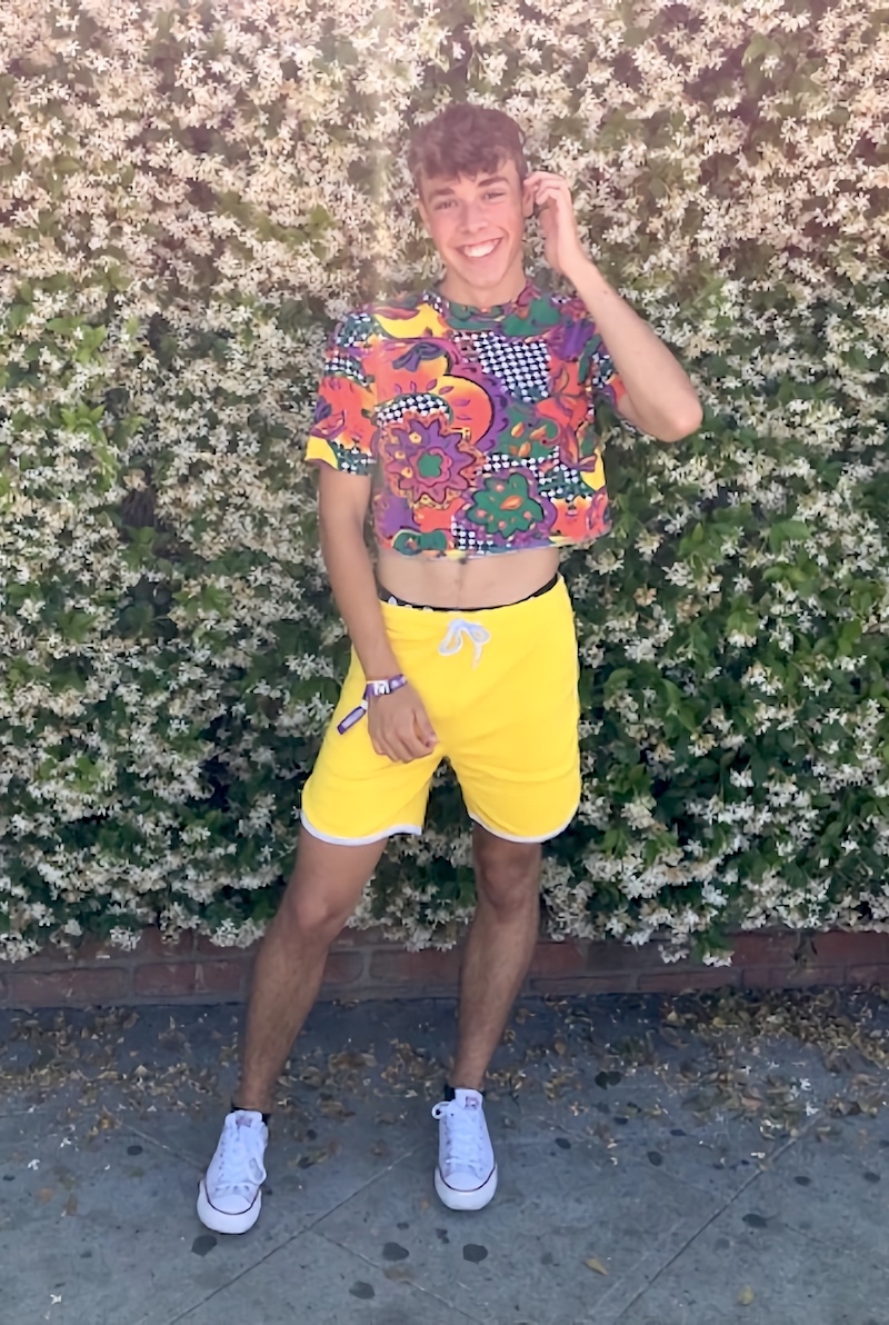 A slightly older man wearing a rainbow crop top and yellow short shorts
