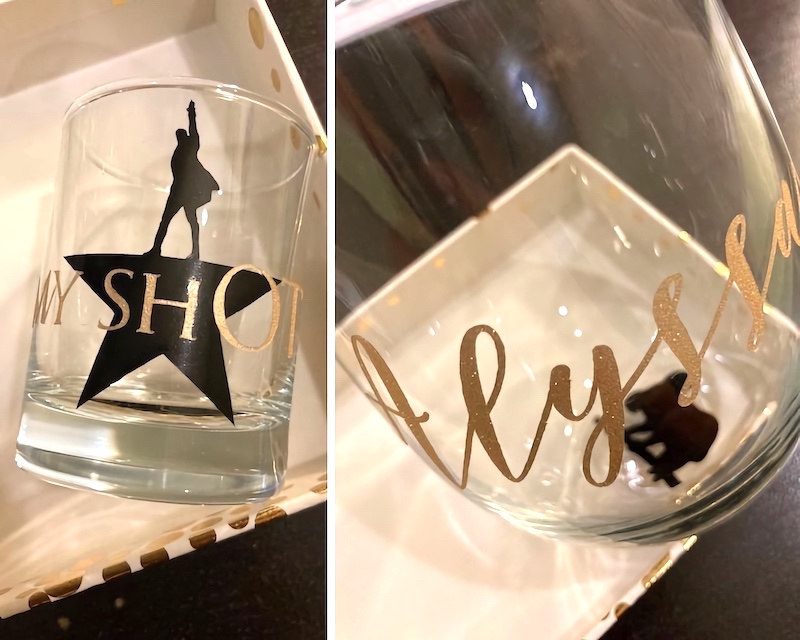 Two images of the final products after Teresa applied the vinyl cuts onto glassware. In the image on the left side, a shot glass reads 'My ShOT,' which is superimposed on top of the Hamilton logo. In the image on the right side, a wine glass reads 'Alyssa,' with the silhouette of a koala hanging onto a tree branch at the bottom of the glass.